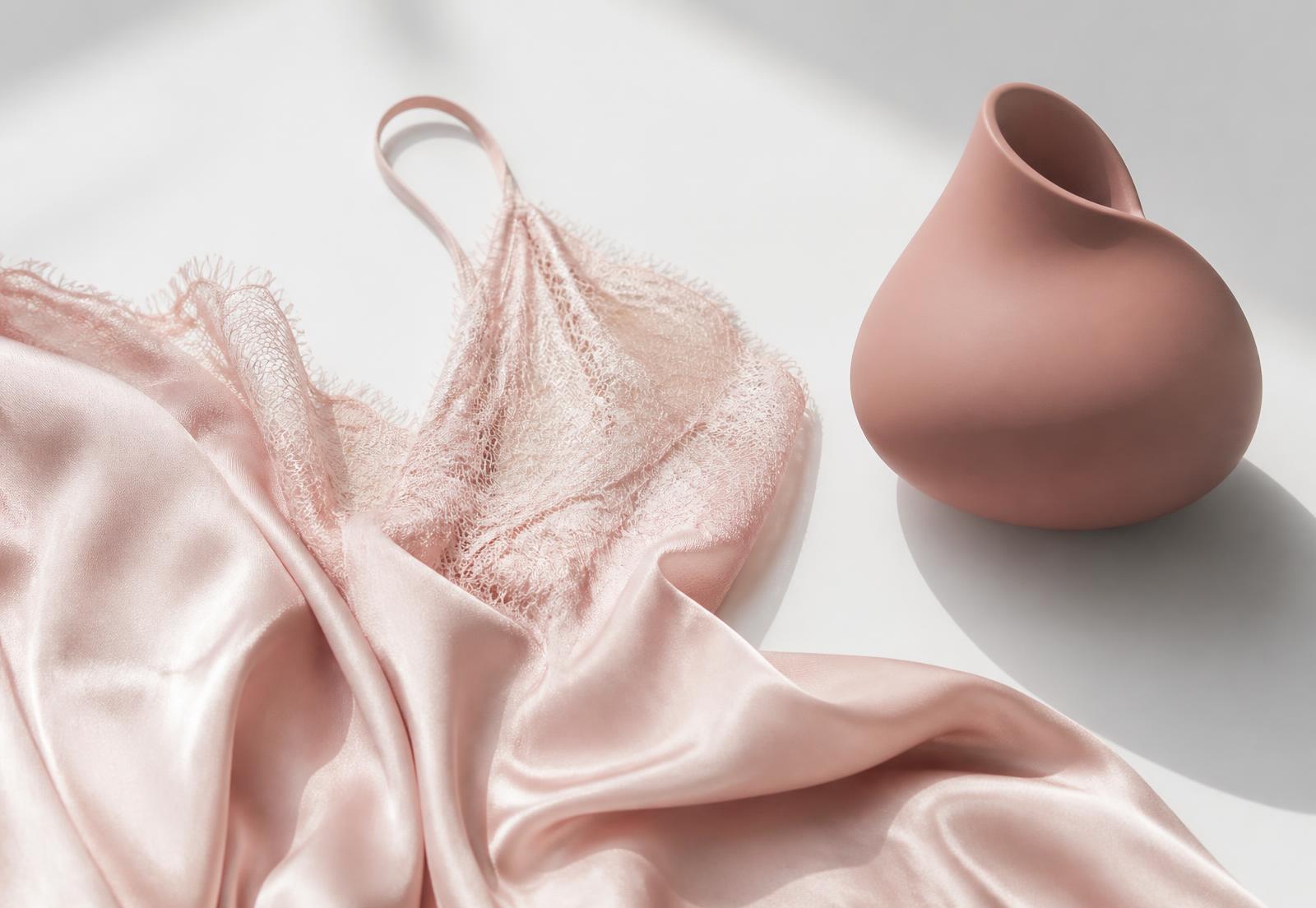 Blush silk lingerie and a minimal rose-toned wellness object on a white surface
